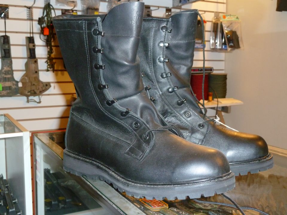 Pair of black leather combat boots with laces, displayed on a glass surface in a store