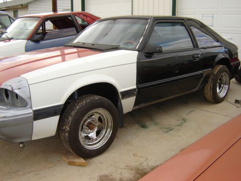 1987 Ford Mustang - A two-tone 1987 Ford Mustang coupe is shown in a side profile, appearing to be under repair.