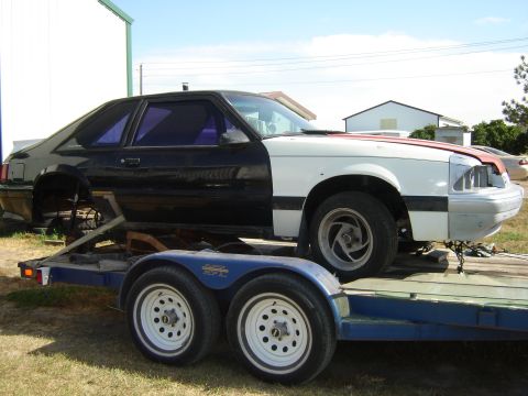 1987 Ford Mustang - A two-tone 1987 Ford Mustang coupe, partially disassembled and loaded onto a trailer for transport.