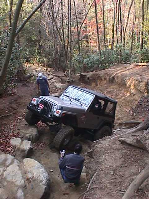 1996 Ford Bronco - A Jeep Wrangler tackles a challenging off-road trail, with a person capturing the action on camera.