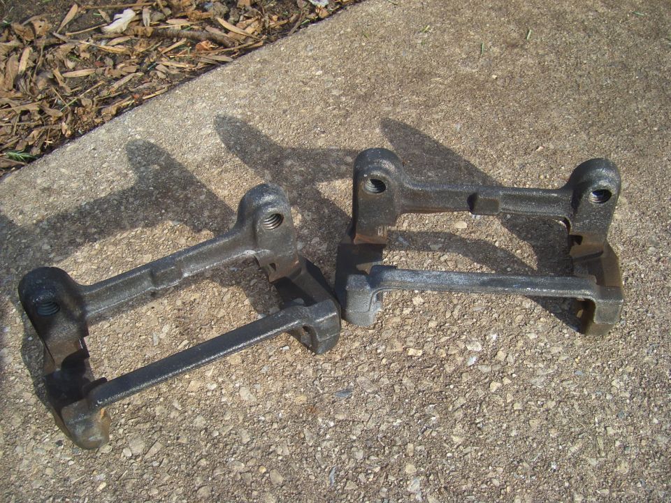 Two dark metal brake caliper brackets on a concrete surface