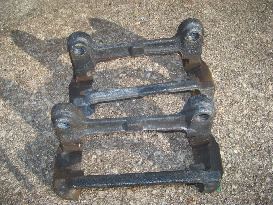Stack of dark metal brake caliper brackets on concrete