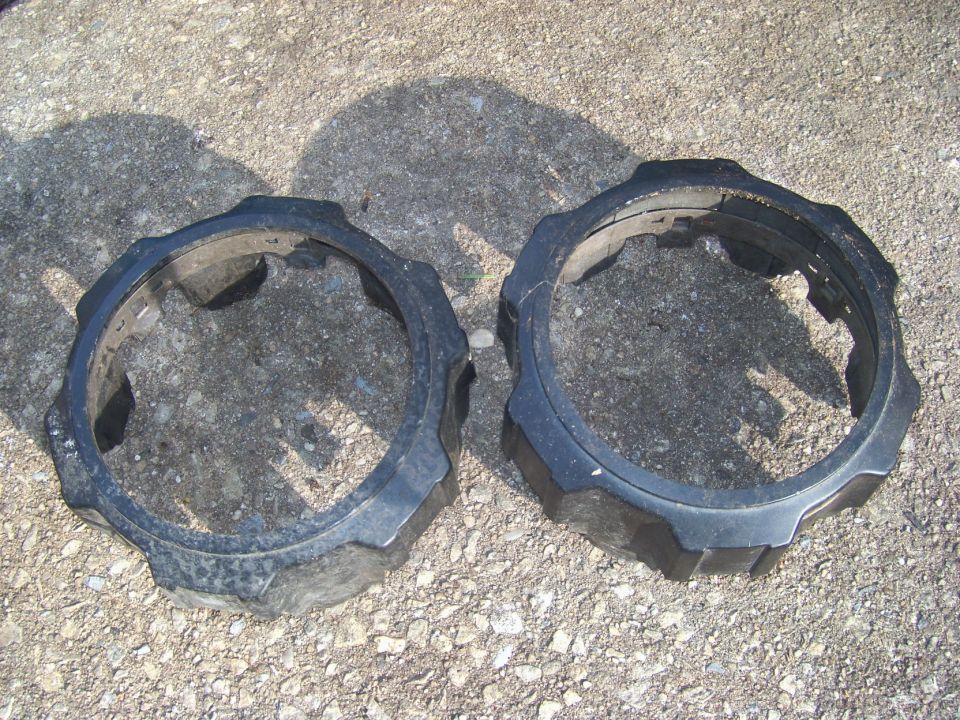 Two black plastic rings with gear-like edges on a gravel surface