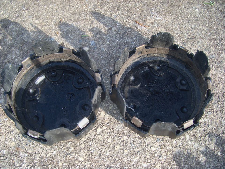 Two black plastic hubcaps with metal clips, lying on gravel