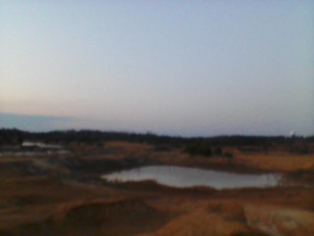 Dirt mounds and water under a pale sky. Supermotors.net logo in the corner