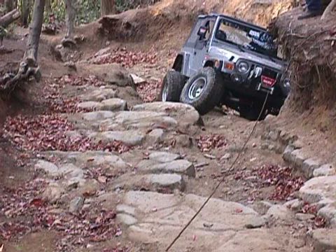 1996 Ford Bronco - A silver Jeep Wrangler TJ navigates a challenging rocky off-road trail, with a winch cable providing assistance.