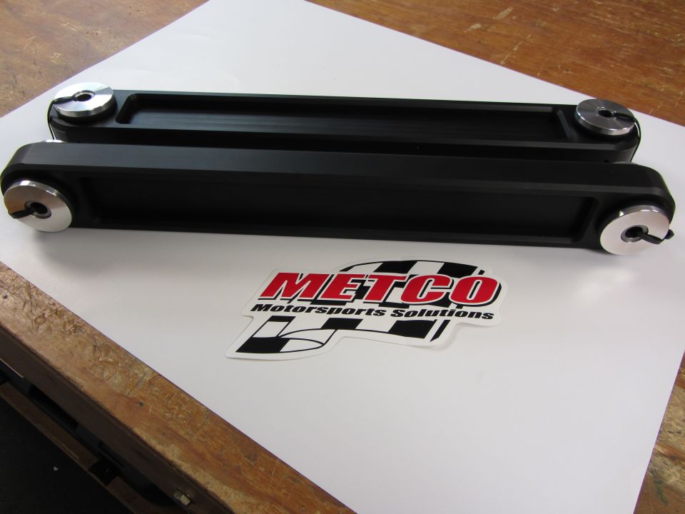 Two black Metco Motorsports Solutions control arms with silver end caps sit on a white surface