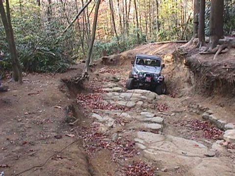 1996 Ford Bronco - A Jeep Wrangler tackles a challenging, rocky off-road path in the woods.
