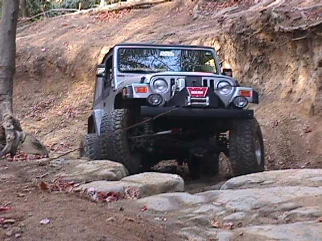 Silver Jeep Wrangler navigating large rocks on a dirt trail