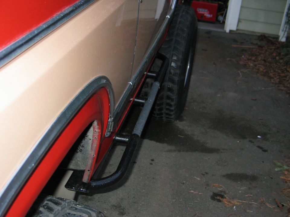 Side view of a 1984 Ford Bronco showing tan paint, red fender flares, and black rock sliders