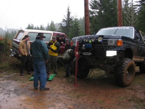 1995 Ford Bronco - Two Ford Broncos, one black and one red, are parked in a muddy, wooded area with several people around them.