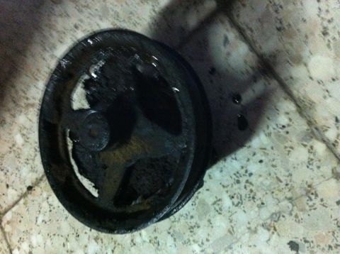 1998 Ford Crown Victoria - A used power steering pump sits on a tiled surface, showing signs of wear and oil residue.