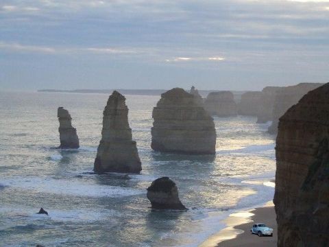 1969 Lincoln Continental - Iconic limestone stacks known as the Twelve Apostles stand against the ocean at sunrise, with waves lapping the sandy beach.