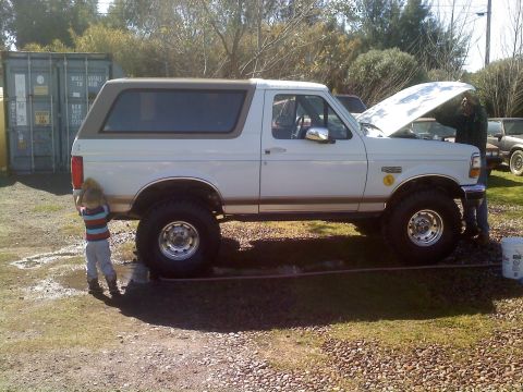 1996 Ford Bronco - A white Ford Bronco is parked outside with its hood up while someone works on the engine. A child stands near the rear tire.