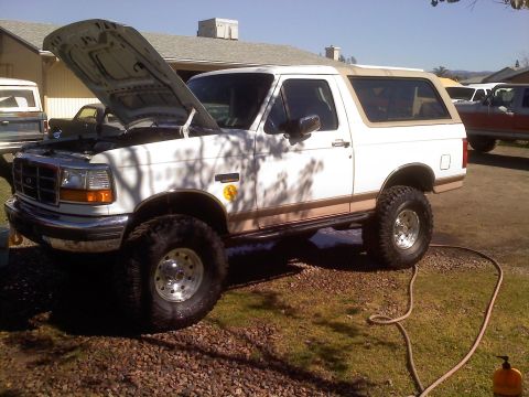1996 Ford Bronco - A white Ford Bronco with a lifted suspension and tan removable top is parked outside with its hood open.