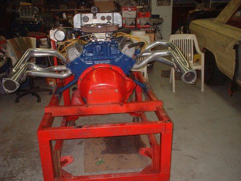 1969 Mercury Cyclone - A V8 engine assembly, a blue block and chrome headers, is mounted on a red stand in a workshop.