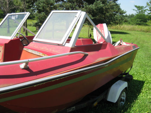 Red boat with two windshields on a trailer in a grassy area