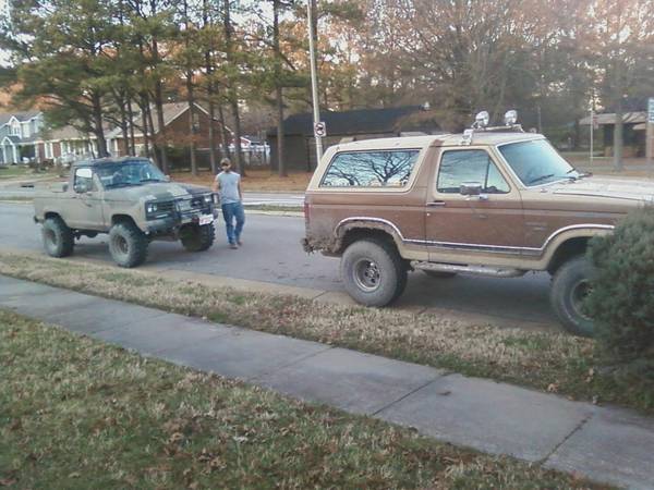 guy standing next to lifted tan pickup truck, brown SUV parked on side of road