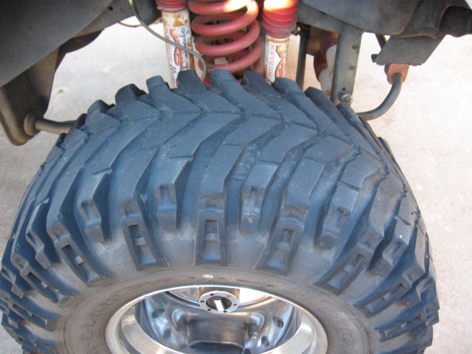 Close-up of a large, knobby off-road tire with red coilover shocks and suspension parts visible above