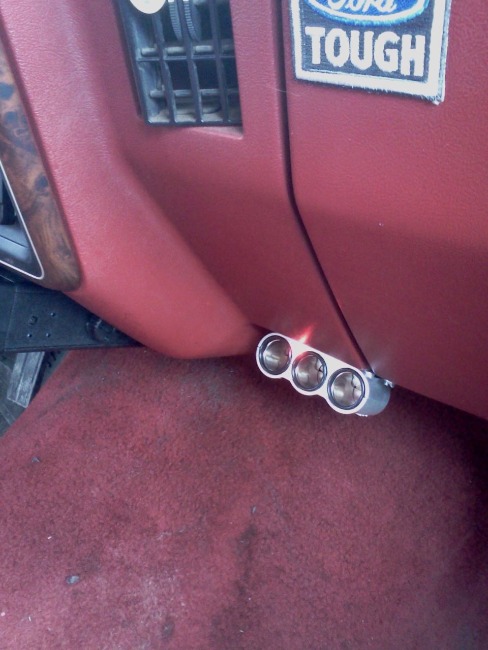 Triple cigarette lighter installed on red dashboard near air vent. Ford Tough sticker visible