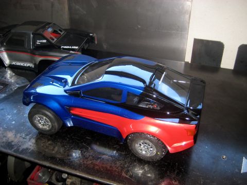 1996 Ford Bronco - Two RC car bodies, one blue and red, the other gray and black, sit on a workbench.