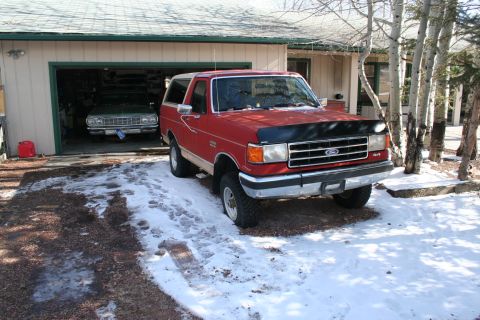 1990 Ford Bronco - A red 1990 Ford Bronco 4x4 is parked in front of a garage, with another vehicle visible inside.