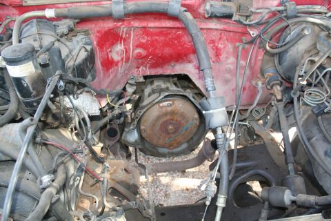1990 Ford Bronco - The engine bay of a vehicle is shown, with the transmission and various hoses and wires visible.
