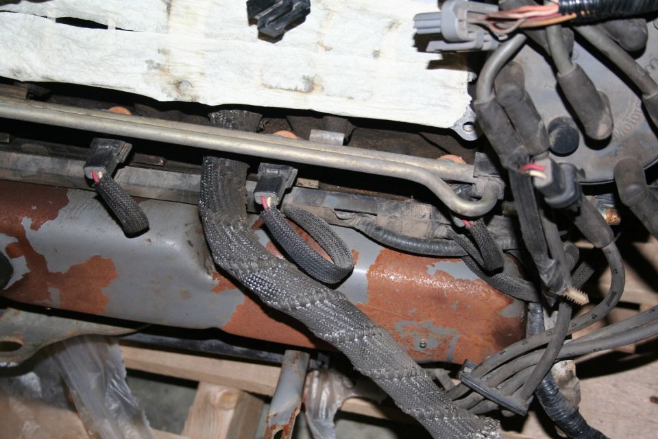 Engine bay showing fuel lines and wiring harness with rust on metal components