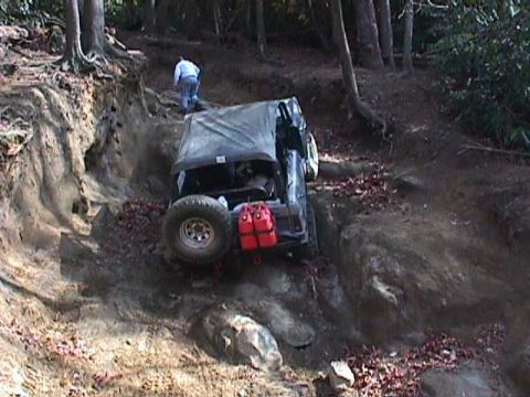 1996 Ford Bronco - An off-road vehicle navigates a challenging dirt trail, with a person walking behind it.