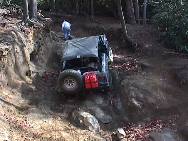 Off-road vehicle with red jerry cans on the back, navigating a steep dirt trail