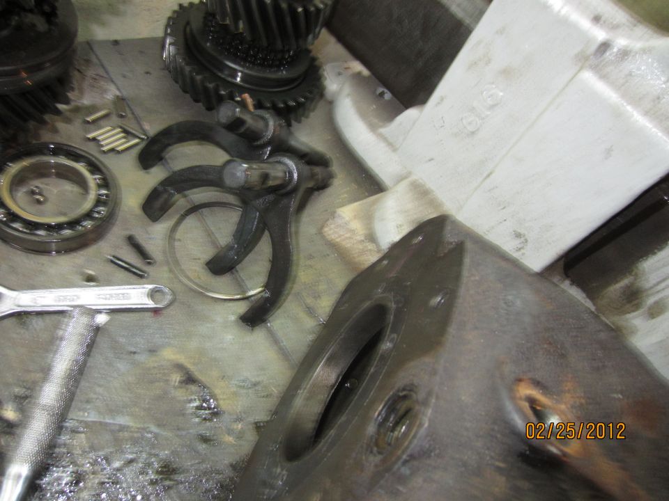 Disassembled transmission parts: gears, bearing, shift forks, pins on a workbench.
