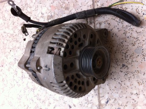 1998 Ford Crown Victoria - This is a used alternator with a ribbed pulley and electrical connector, shown against a speckled background.