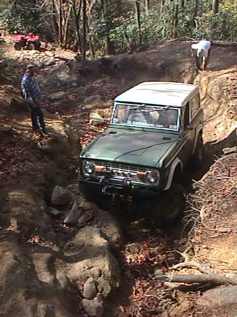 1996 Ford Bronco - A green Ford Bronco tackles a challenging off-road course in a wooded area.