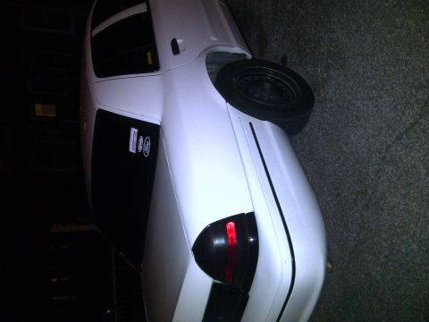 2000 Ford Crown Victoria - A white sedan is parked on a street at night, showing its rear passenger side with a spare tire.