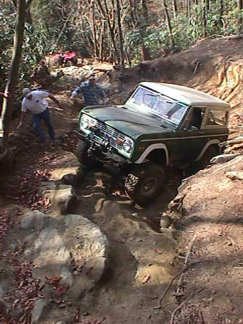 1996 Ford Bronco - A green 1996 Ford Bronco tackles a challenging rocky trail in a wooded area.