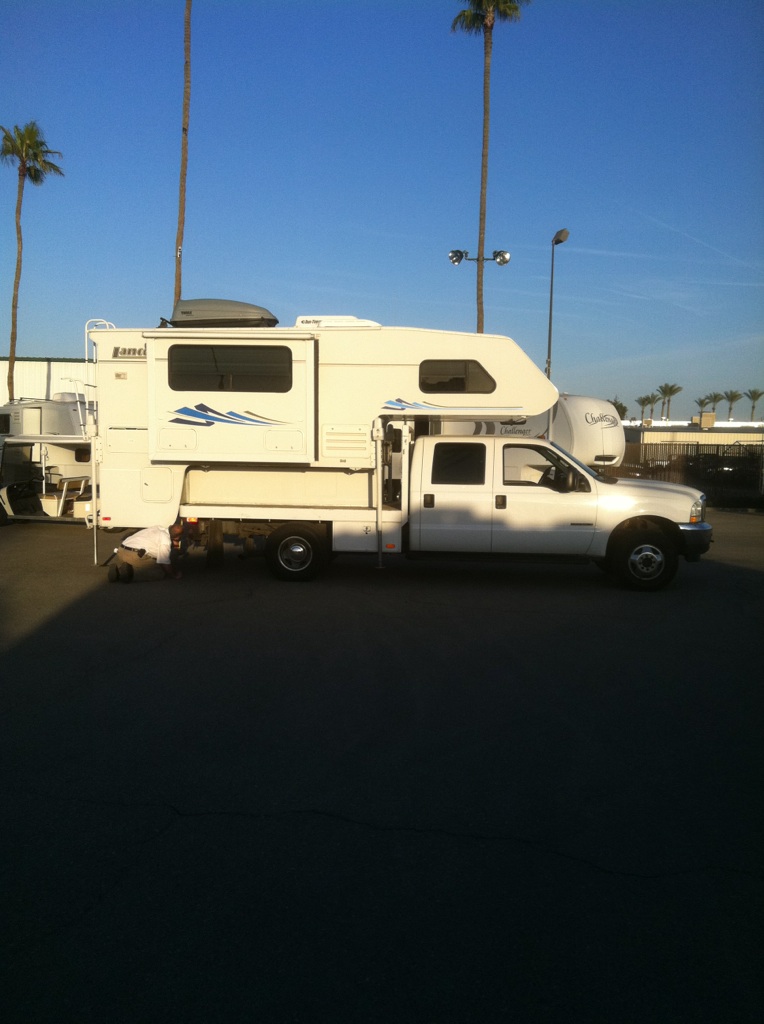 White Ford Super Duty crew cab dually with Lance slide-in camper, side view in palm-lined lot