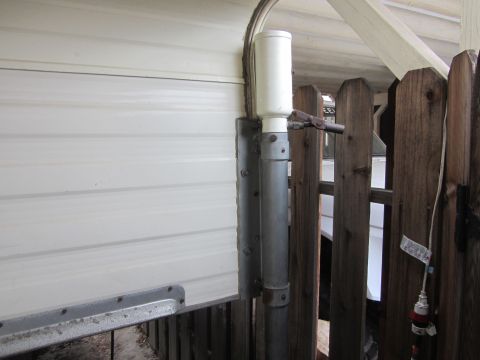 1986 Yugo GV - A close-up view of white siding and a wooden fence with a plumbing pipe and electrical cord visible.