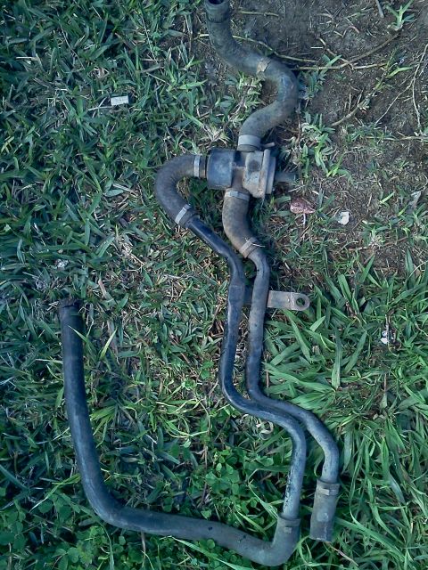 1989 Ford Bronco - Engine coolant hoses with a valve are shown lying on the grass.