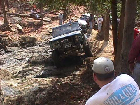 1996 Ford Bronco - Multiple off-road vehicles navigate a challenging rocky and muddy trail in a wooded area.