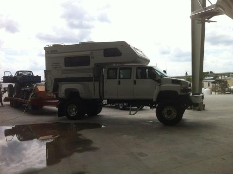 1993 Ford Bronco - A large white custom truck with a camper shell is seen towing a trailer carrying another pickup truck.