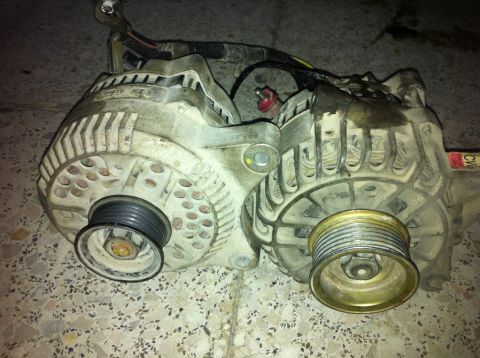 1998 Ford Crown Victoria - Two automotive alternators are shown, one with a brass pulley and the other with a black pulley.