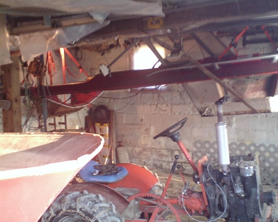 Red tractor with chains on tires, steering wheel, and engine visible in a garage