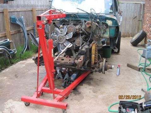1979 Ford Bronco - A green vehicle is disassembled and supported by an engine hoist, with its engine compartment fully exposed.