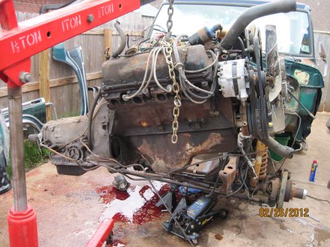 1979 Ford Bronco - Engine and transmission assembly is being removed from a vehicle, with fluid spilled on the ground.