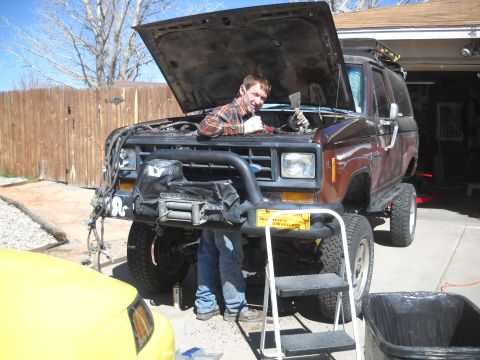 1992 Ford Explorer - Man performs maintenance on a lifted Ford Bronco II in a driveway, with a yellow car nearby.