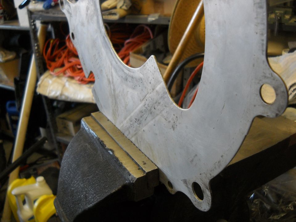 Metal bracket clamped in a vise, with "SUPERMOTORS.NET" visible at the bottom right