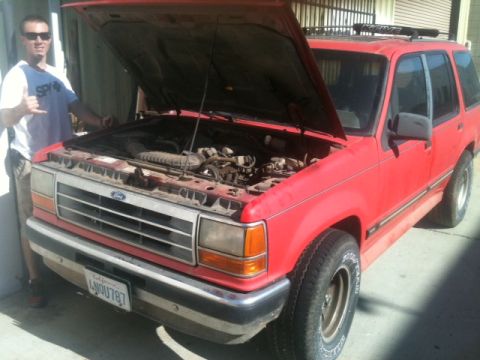 1988 Ford Bronco II - A man stands by a red Ford Explorer with its hood up, revealing the engine compartment.