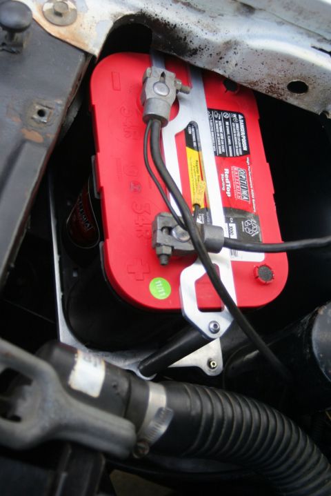 1976 Ford Ranchero - Close-up view of a red car battery with visible text and wiring in an engine compartment.