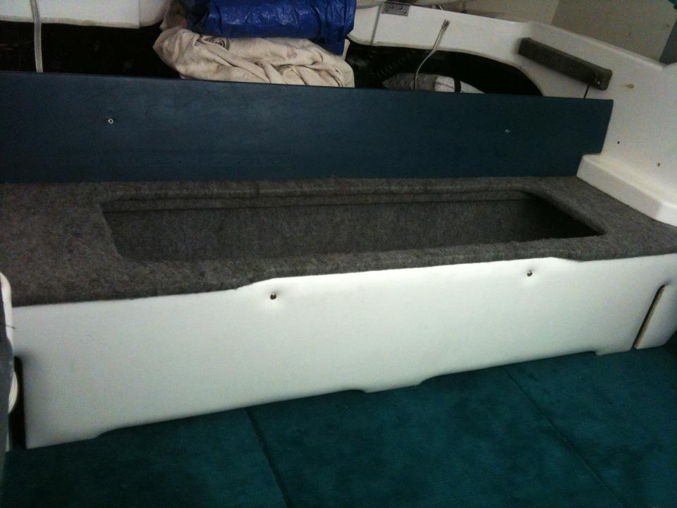 Boat interior with white and blue upholstered seating and a carpeted storage compartment
