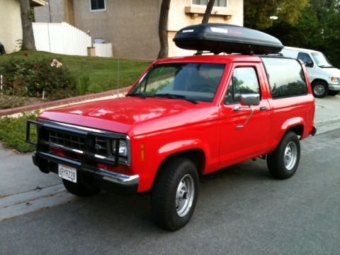 1988 Ford Bronco II - Red 1988 Ford Bronco II parked on a street, with a white van in the background.